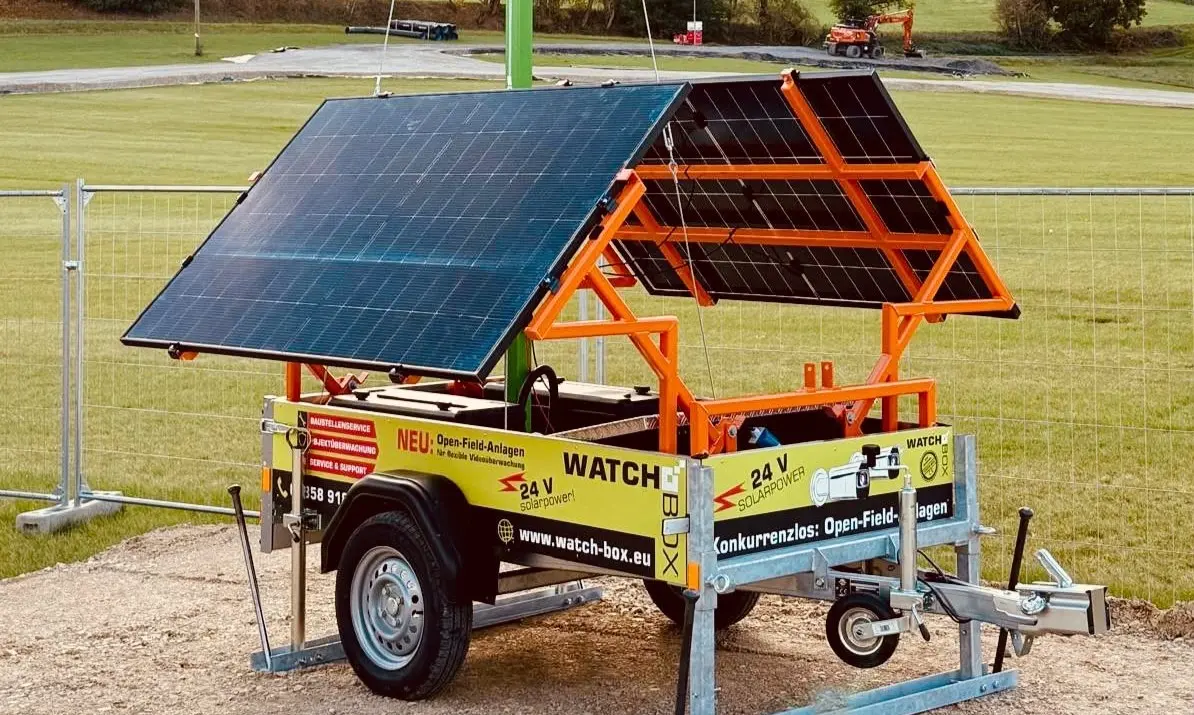 Mobiler gelber Anhaenger mit Solarpanelen fuer Videoueberwachung auf Wiese